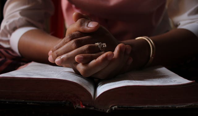 Close-up of a person praying with hands clasped over an open Bible, highlighting devotion.