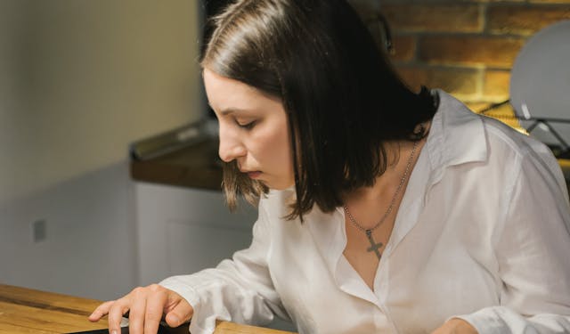A woman studies the Bible at a wooden table, combining printed and digital texts.