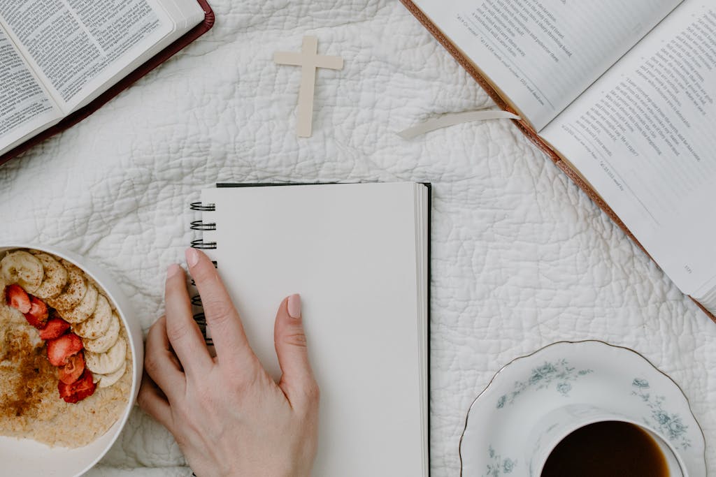 Top view of a morning devotional setup with bible, coffee, and notebook on a cozy textile background.