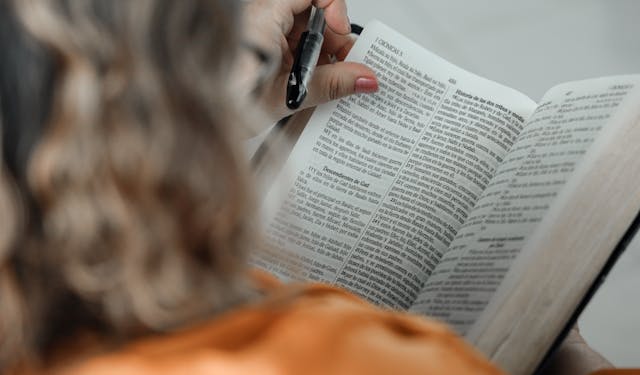 Close-up of a woman reading a Bible with a pen, focused on text.