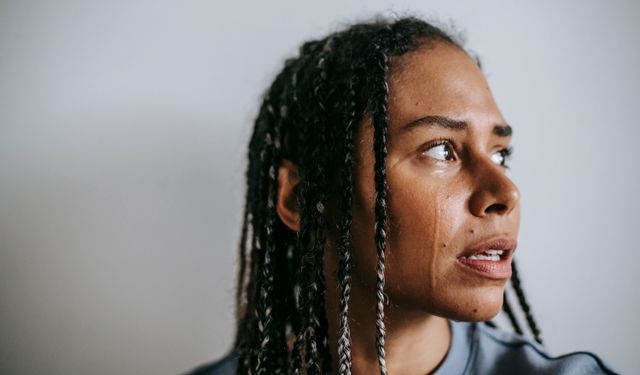 Grieved depressed African American female with dreadlocks crying hopelessly and looking away in dismay against white wall