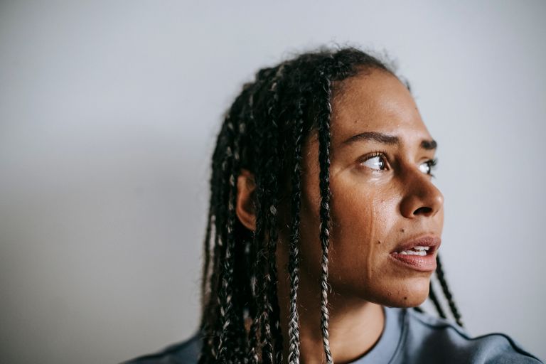 Grieved depressed African American female with dreadlocks crying hopelessly and looking away in dismay against white wall
