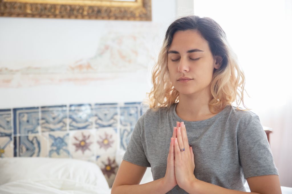 Peaceful woman meditating indoors, eyes closed, in a serene environment.