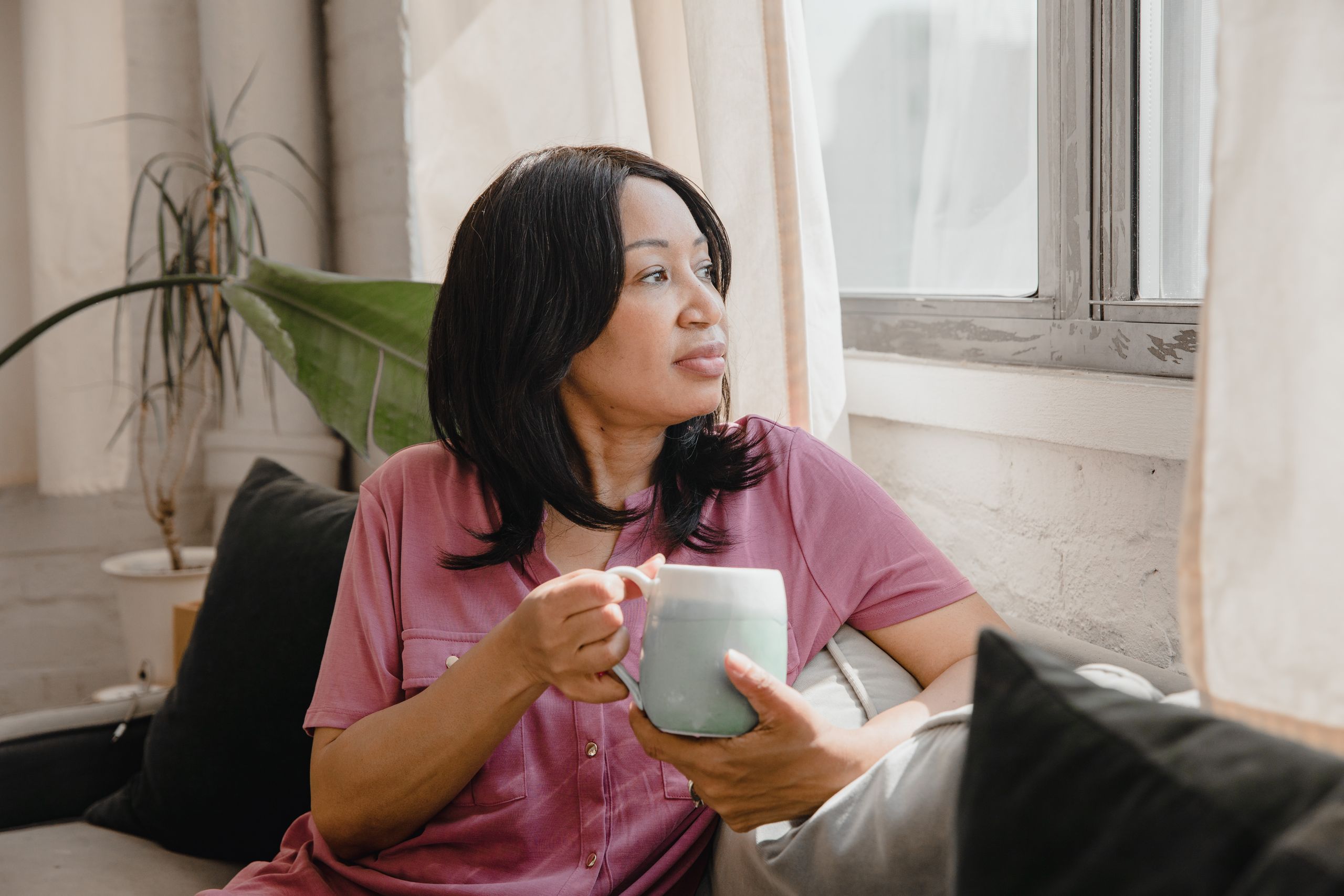 Woman enjoying a quiet moment with coffee, looking out the window.